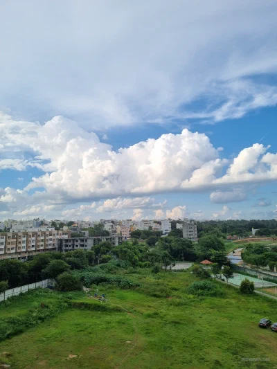 Clouds above apartment buildings and a green field