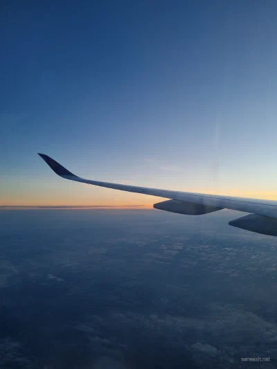 An airplane wing above clouds in the fading light