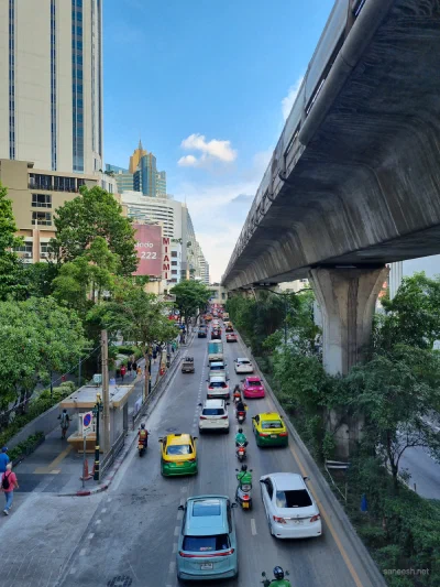 Traffic moving along a city street beside an elevated railway
